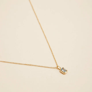 Gold birthstone pendant necklace on a beige background. 