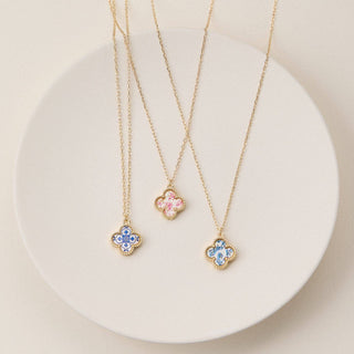 Gold necklaces with clover pendants on a light beige background