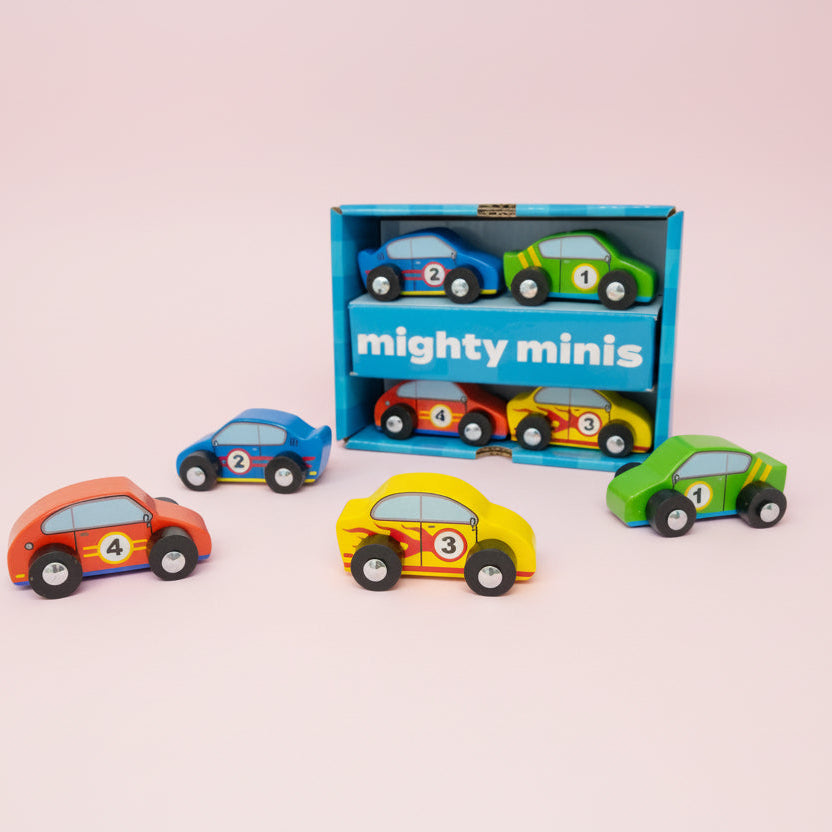 Set of colorful toy cars in front of a 'mighty minis' box on a pink background