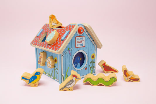 Wooden toy birdhouse with detachable bird pieces on a pink background