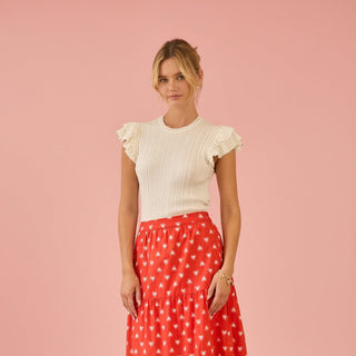Woman wearing a white top and red polka dot skirt on a pink background