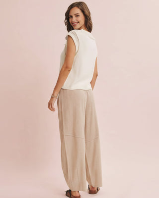 Woman wearing a white sleeveless top and beige wide-leg pants on a pink background