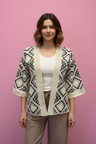 model wearing a patterned cardigan over a white shirt and brown pants on a pink background