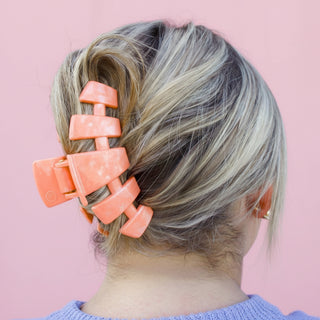 Person with a coral hair clip against a pink background