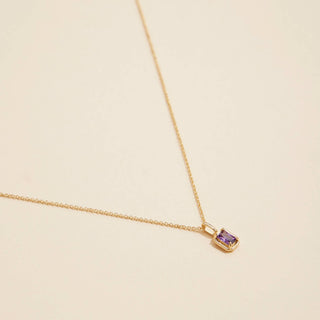 Gold birthstone pendant necklace on a beige background. 