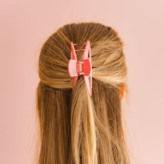Person with a red hair clip in their hair against an pink background