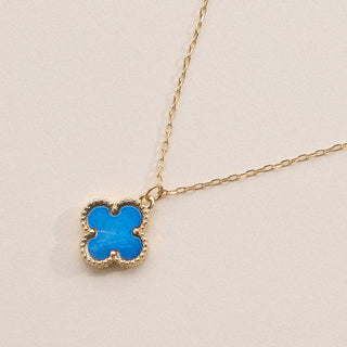 Gold necklace with a clover pendant on a light pink background
