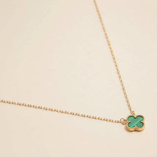 Gold necklace with a green clover-shaped pendant on a beige background