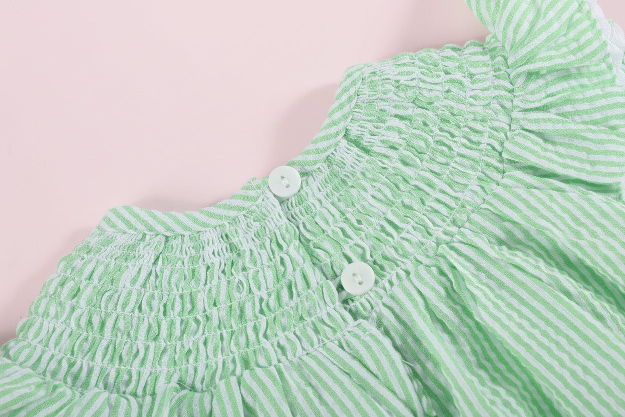 Green and white striped baby outfit with smocked details on a light pink background
