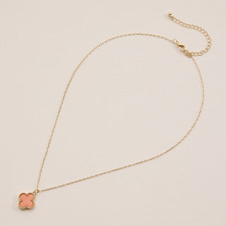 Gold necklace with a clover pendant on a light pink background