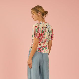 Woman wearing a floral top and light blue pants on a pink background