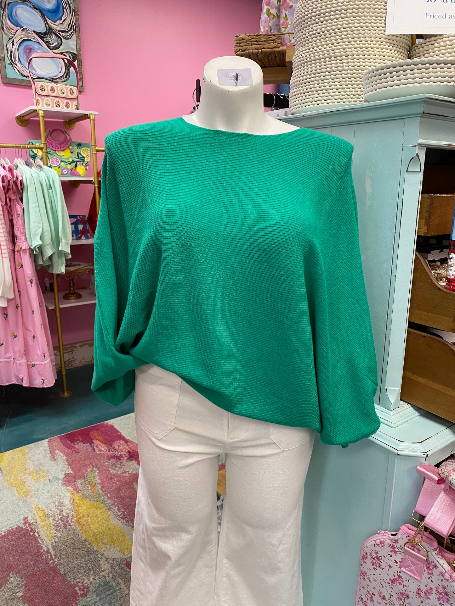 Mannequin wearing a green top and white pants in a store setting with pink walls and various items in the background.