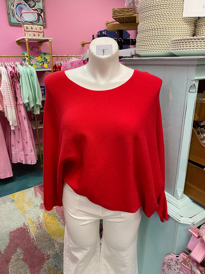 Mannequin wearing a red sweater and white pants in a store setting with pink walls and clothing racks.