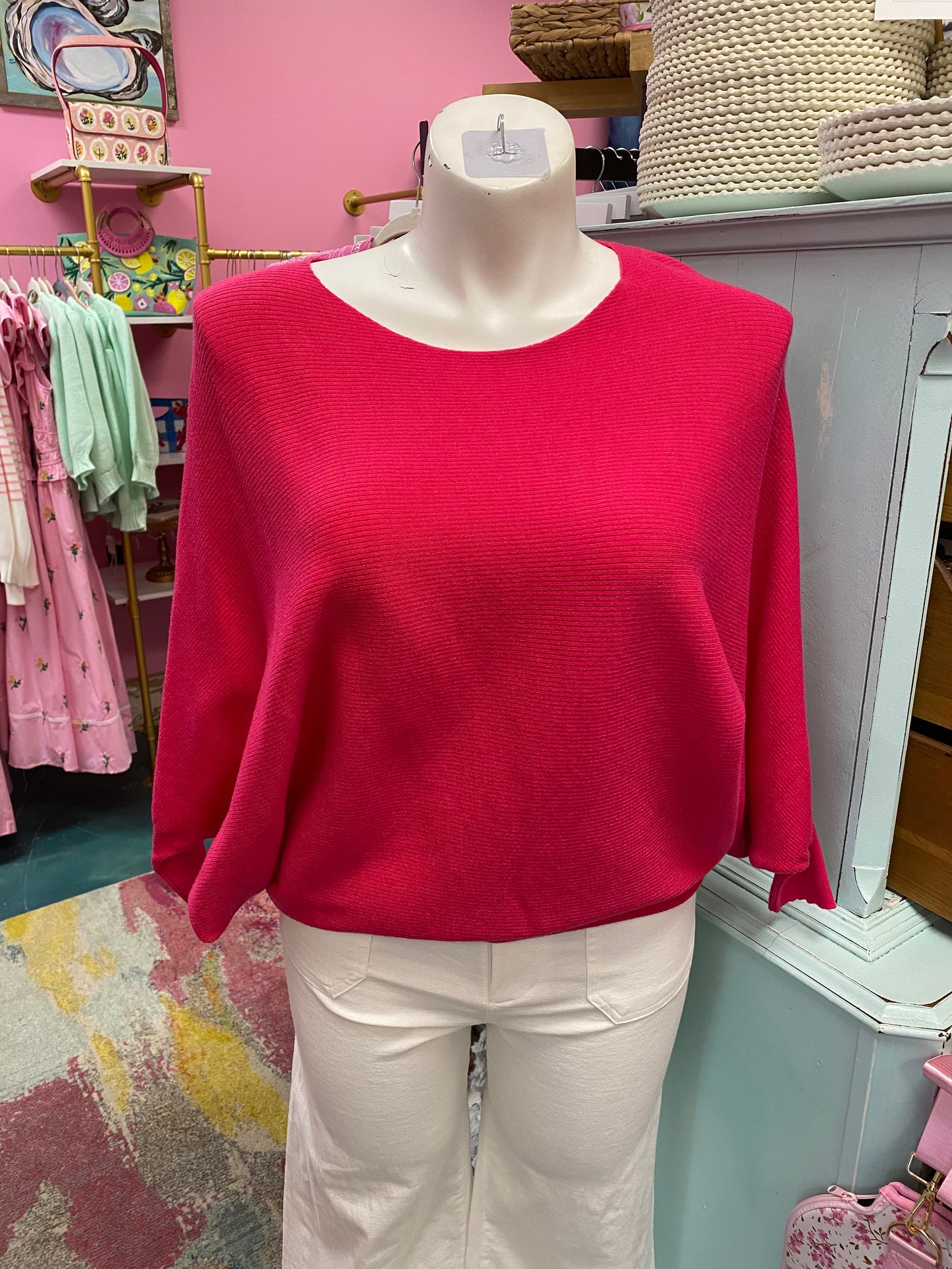 Red sweater on a mannequin in a store setting with pink walls and clothing racks.