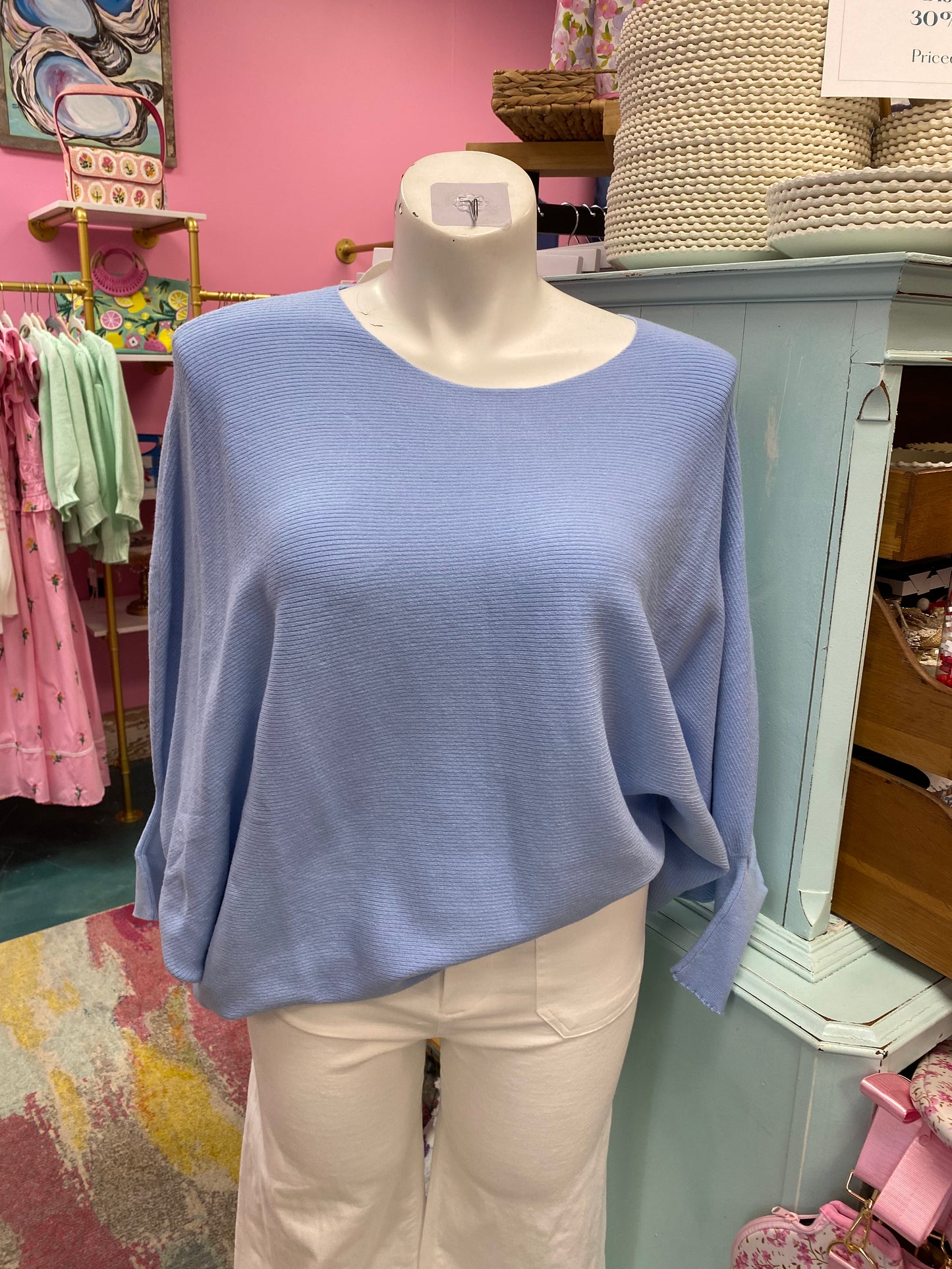 Blue sweater on a mannequin in a store setting with pink walls and various items in the background.