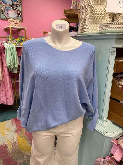 Blue sweater on a mannequin in a store setting with pink walls and various items in the background.