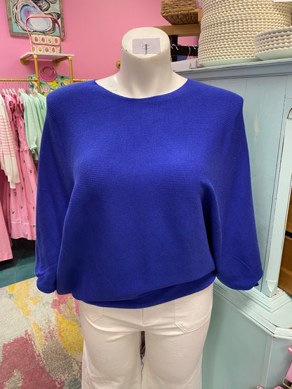 Blue sweater on a mannequin in a store setting with pink walls and various items in the background