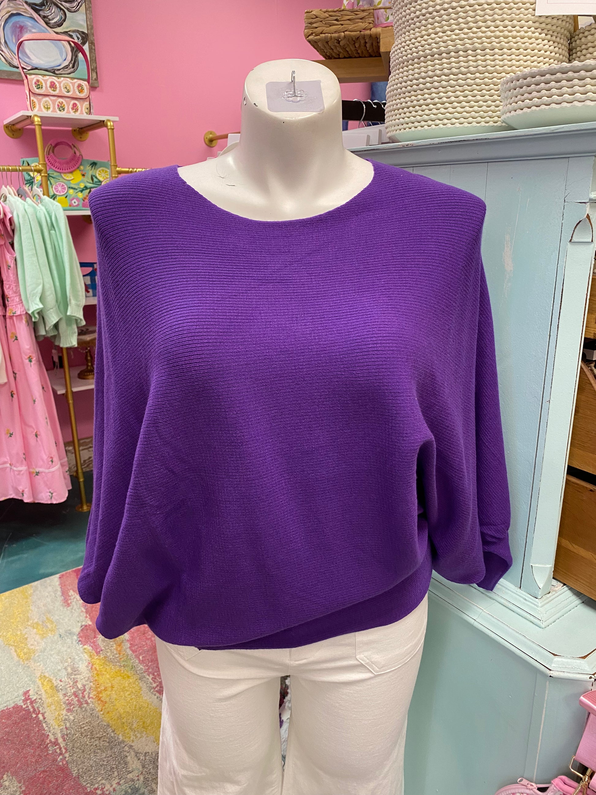 Purple sweater on a mannequin in a store setting with pink walls and various items in the background.
