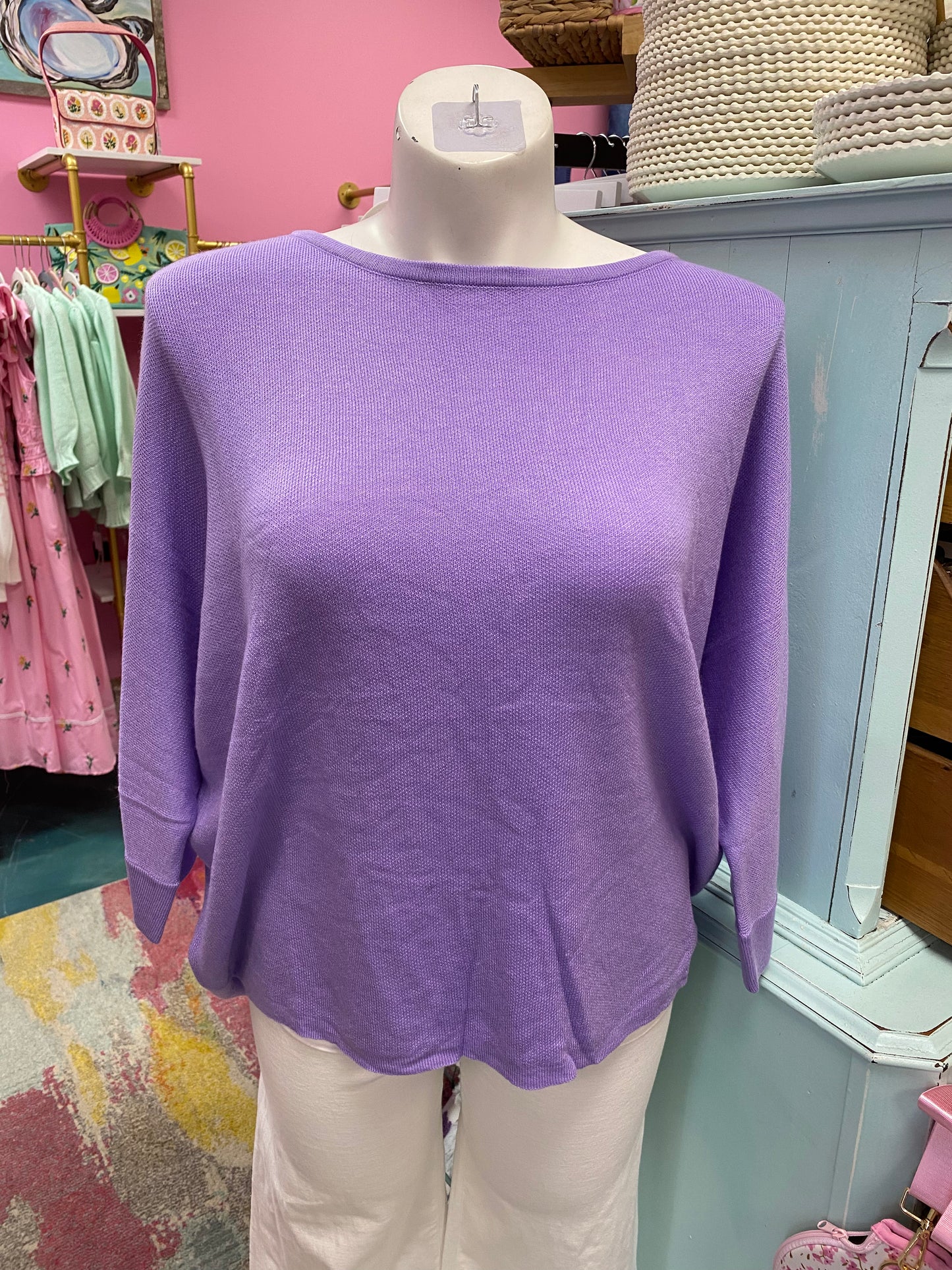 Purple sweater on a mannequin in a store setting with pink walls and various items in the background.