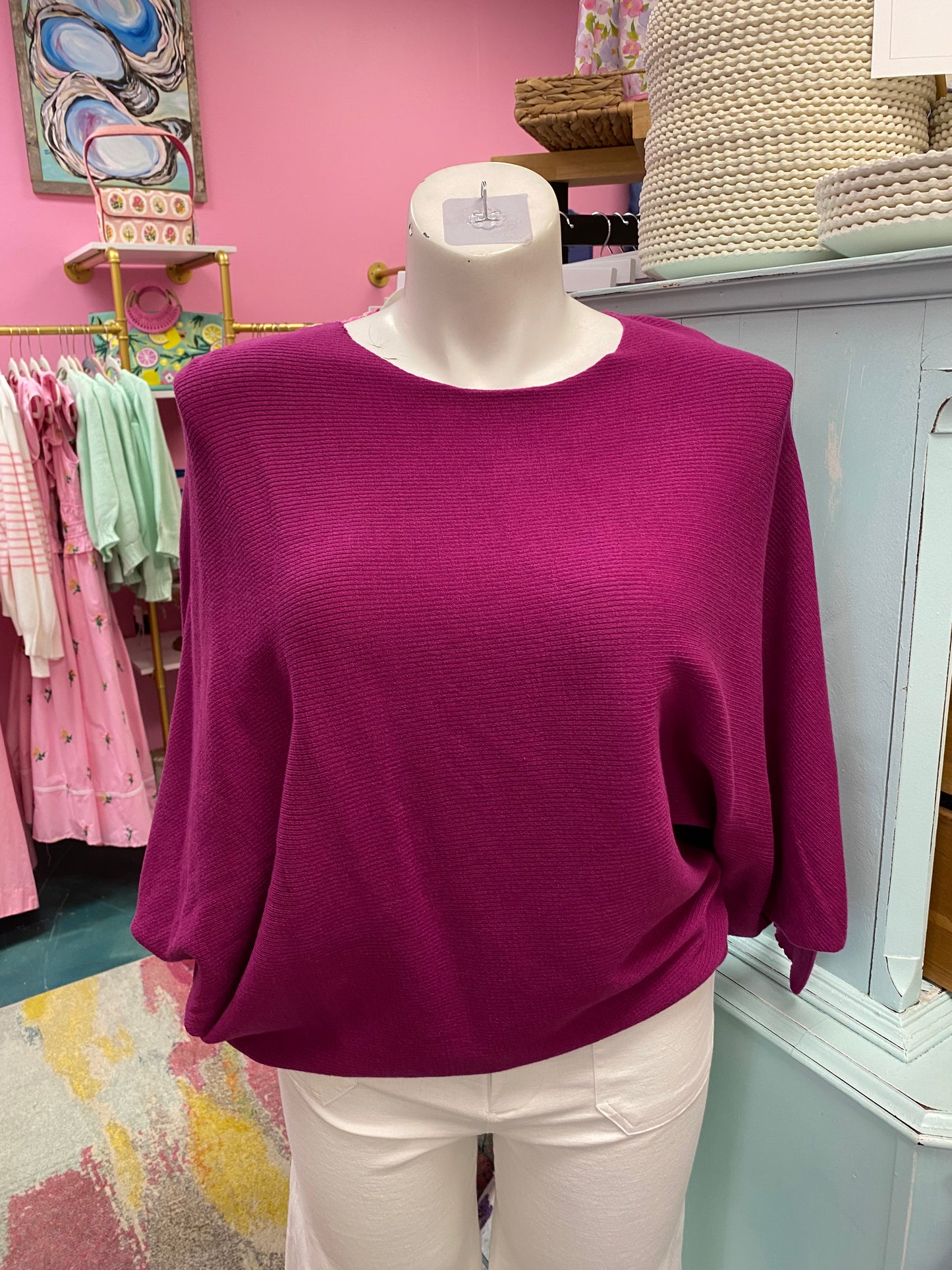Purple sweater on a mannequin in a store setting with pink walls and clothing racks.