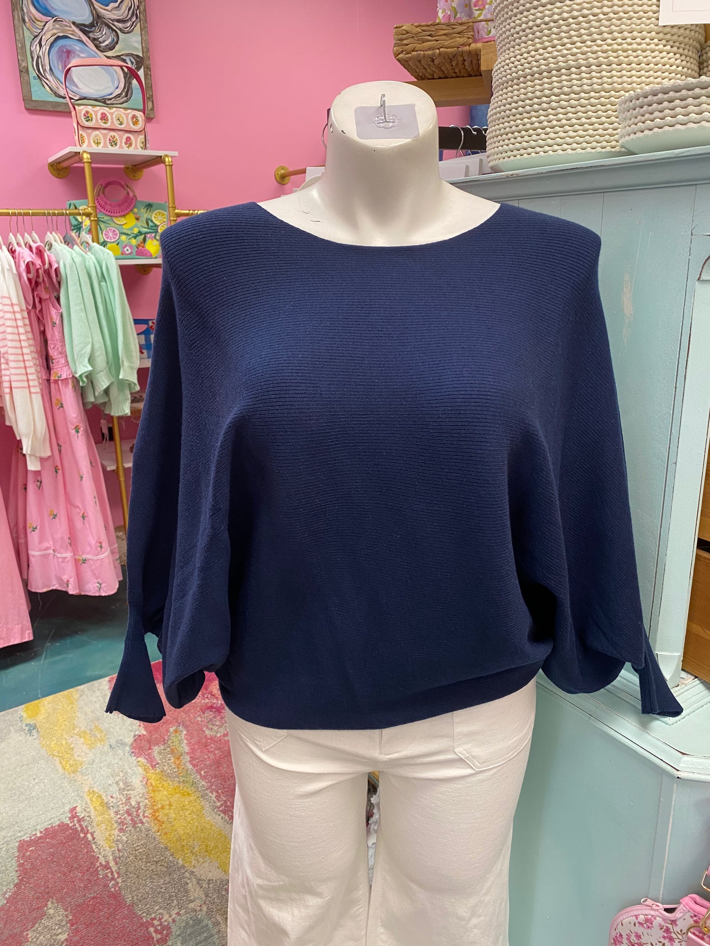 Navy sweater on a mannequin in a store setting with pink walls and various items in the background.