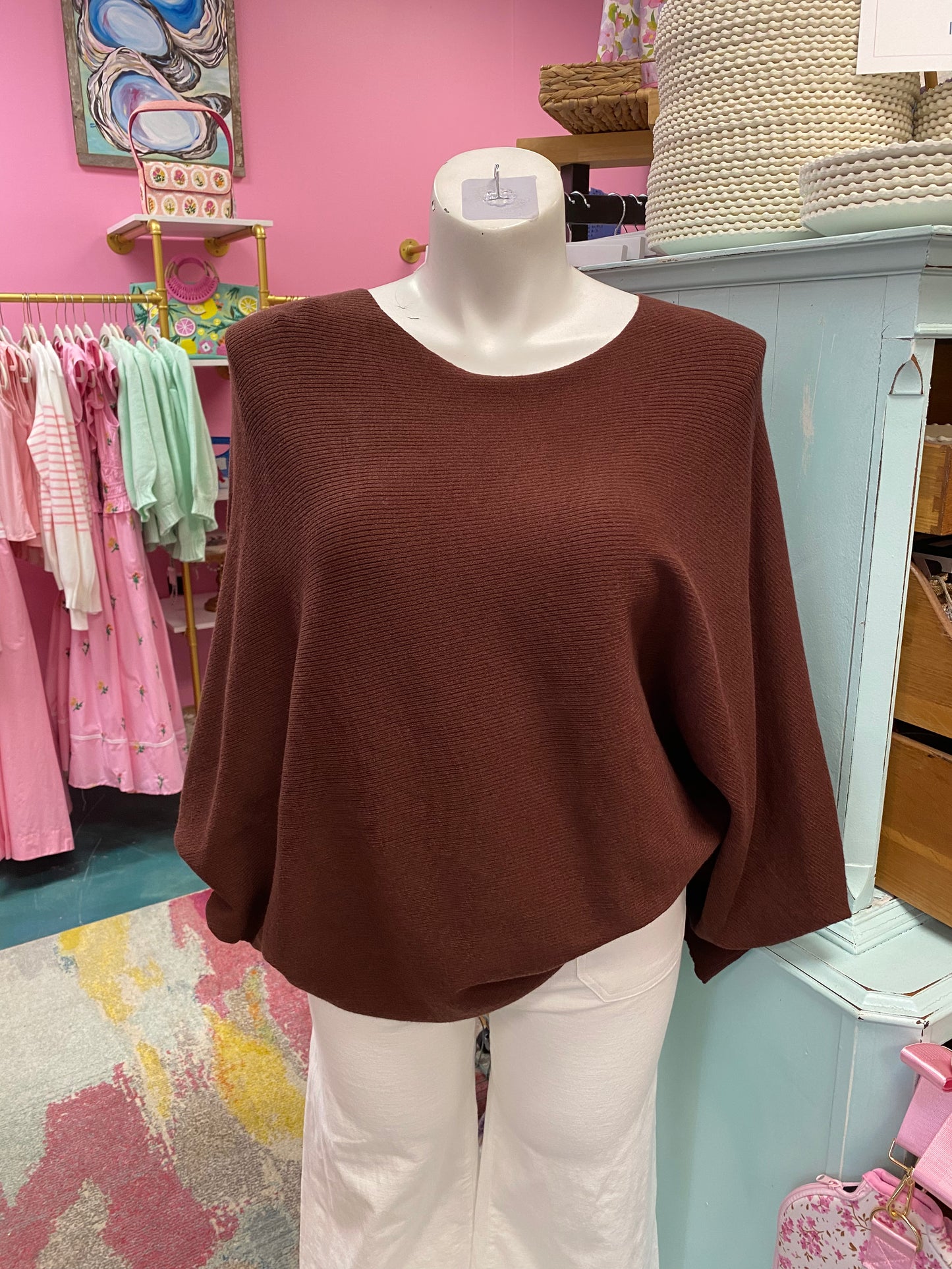 Brown sweater on a mannequin in a store setting with pink walls and various items in the background.
