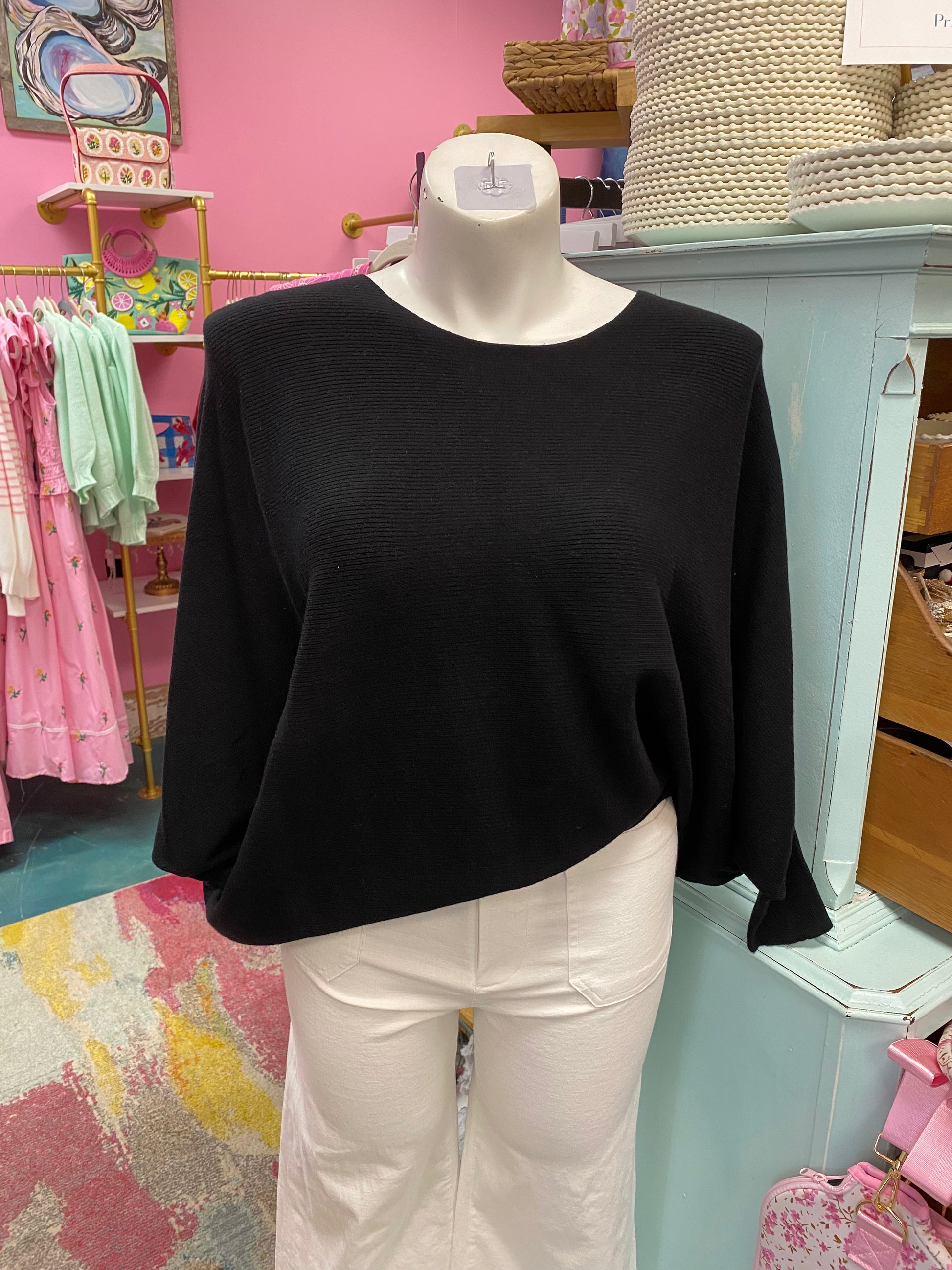 Black sweater on a mannequin in a store setting with pink walls and various items in the background.