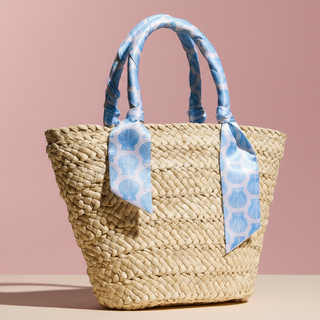 Woven straw bag with blue patterned handles on a pink background