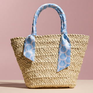 Woven straw bag with blue patterned handle on a pink background