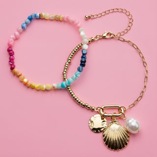 Two bracelets on a pink background, one with colorful beads and the other with gold chain and shell charm.