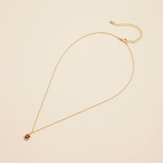 Gold birthstone pendant necklace on a beige background. 