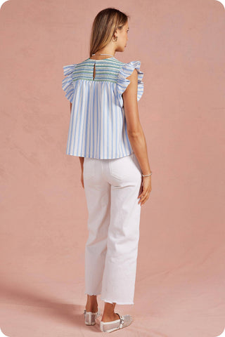 Woman wearing a blue and white striped top with ruffled sleeves on a pink background