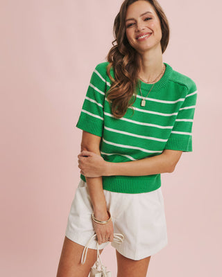 Woman wearing a green and white striped sweater with white shorts on a pink background