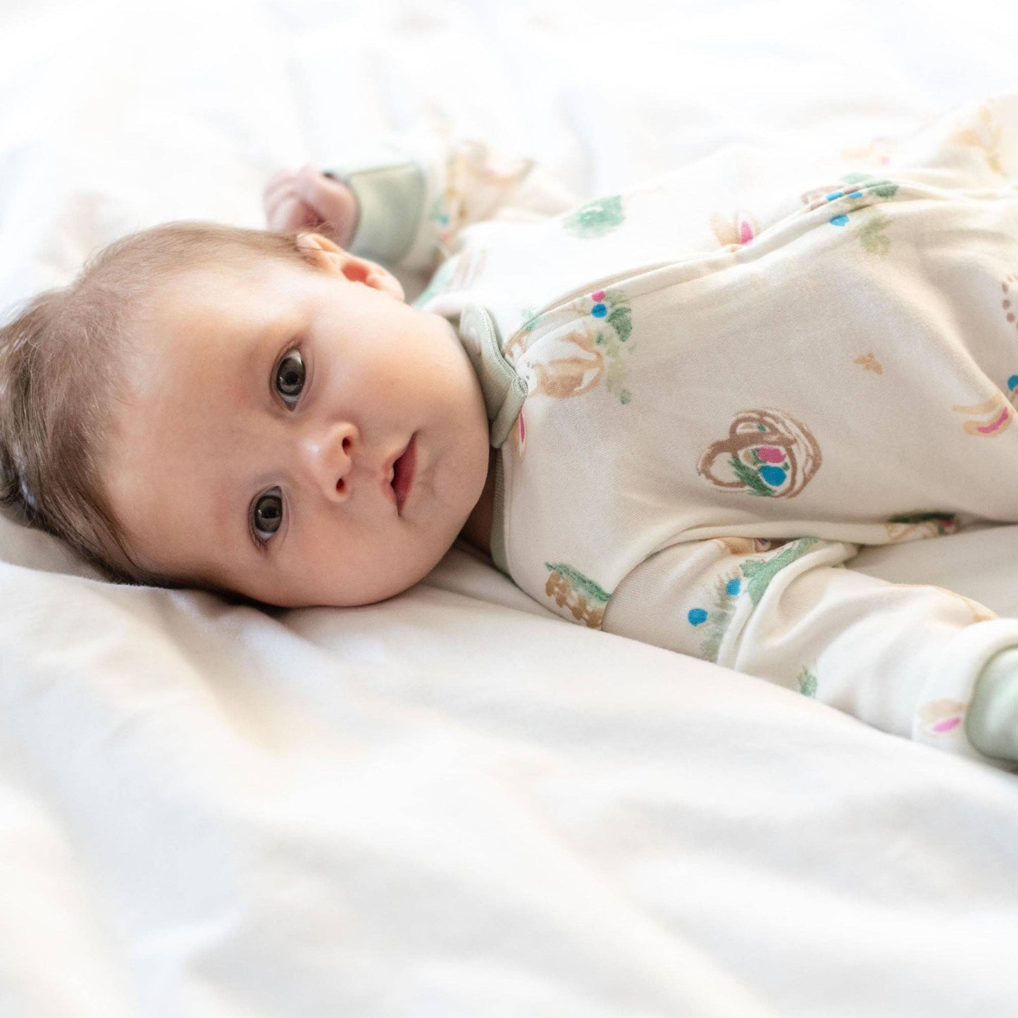 Baby lying on a white blanket wearing a patterned outfit.