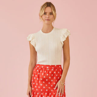 Woman wearing a white top with ruffled sleeves and a red polka dot skirt on a pink background