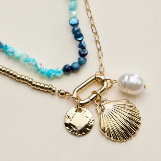 Jewelry set with gold chain, shell charm, and pearl on a light background