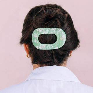 Person with a floral green hair clip in their hair against a plain background