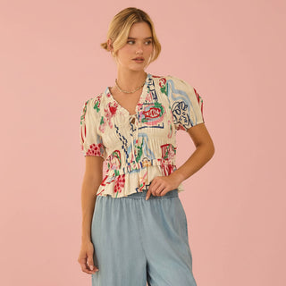Woman wearing a colorful patterned shirt and light blue pants on a pink background