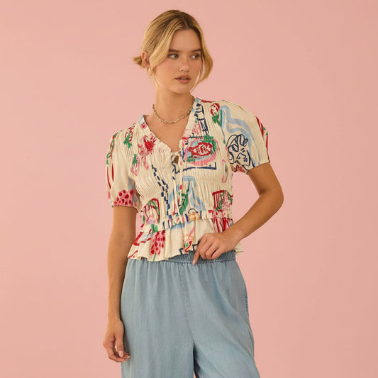 Woman wearing a colorful patterned shirt and light blue pants on a pink background