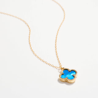 Gold necklace with a clover pendant on a light pink background
