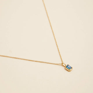 Gold birthstone pendant necklace on a beige background. 