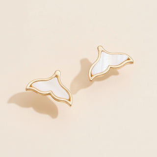 Pair of gold and white whale-shaped earrings on a pink background
