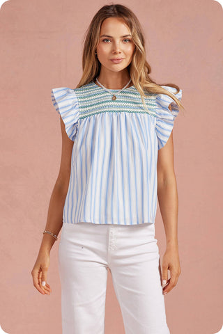 Woman wearing a blue and white striped top with ruffled sleeves against a pink background