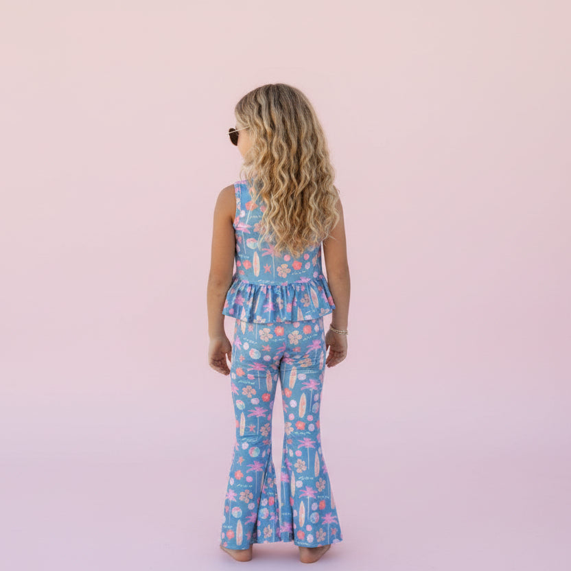 Child wearing a blue floral jumpsuit against a pink background. 