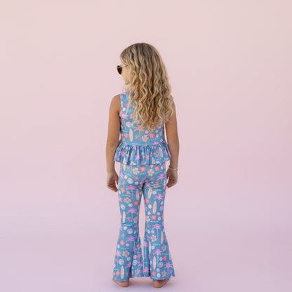 Child wearing a blue floral jumpsuit against a pink background. 