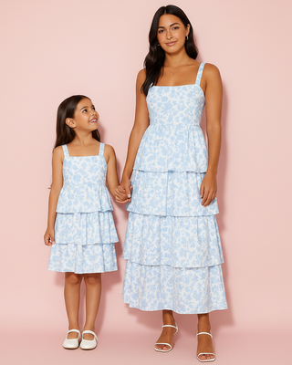 Two women in matching light blue floral dresses standing against a pink background