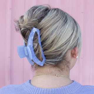 Person with a blue hair clip in their hair against a pink background