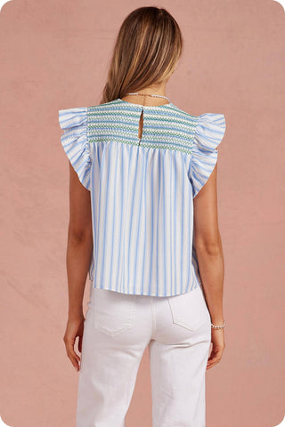 Woman wearing a blue and white striped top with ruffled shoulders on a pink background