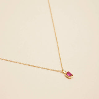 Gold birthstone pendant necklace on a beige background. 