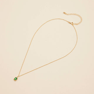 Gold birthstone pendant necklace on a beige background. 